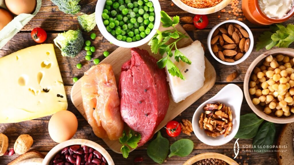 Variedad de alimentos ricos en proteínas sobre mesa rústica, incluyendo carne, pescado, queso, legumbres y frutos secos