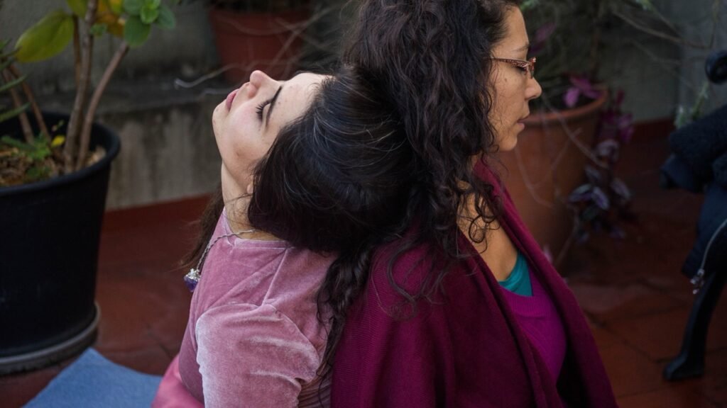 Dos mujeres sentadas de espaldas apoyadas una sobre la otra con los ojos cerrados en gesto de confianza y conexión. Fotografia de Micaela Burgos