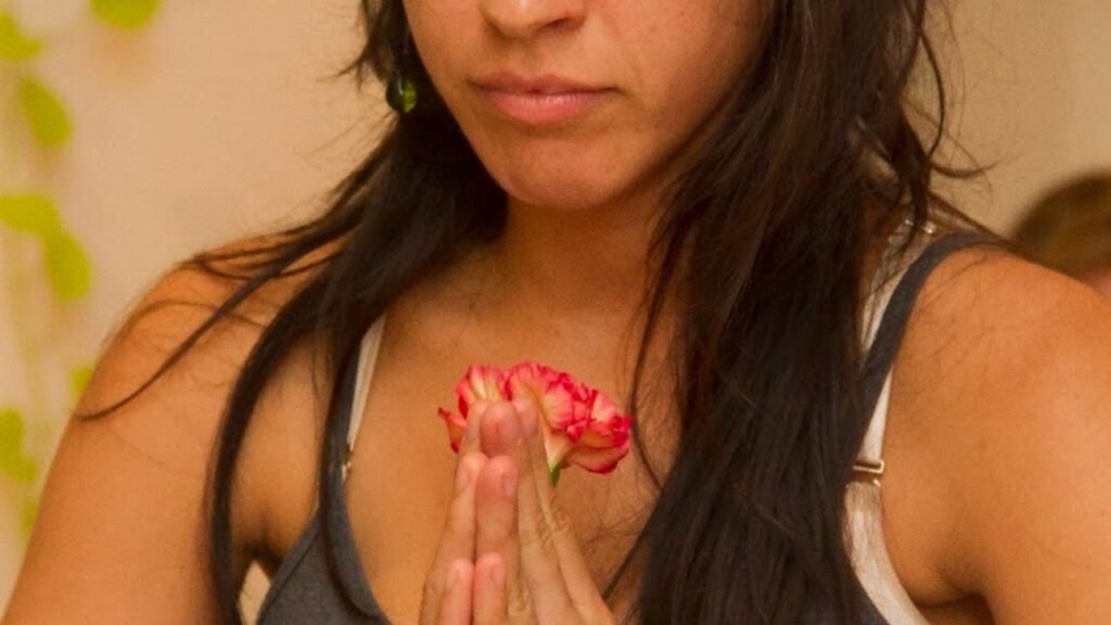 Mujer sosteniendo una flor roja con las manos en posición de oración cerca del pecho