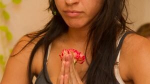 Mujer sosteniendo una flor roja con las manos en posición de oración cerca del pecho
