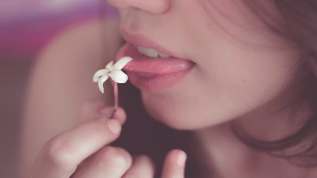 Primer plano de una mujer acercando una pequeña flor blanca a sus labios. Fotografia de Mora Lopez