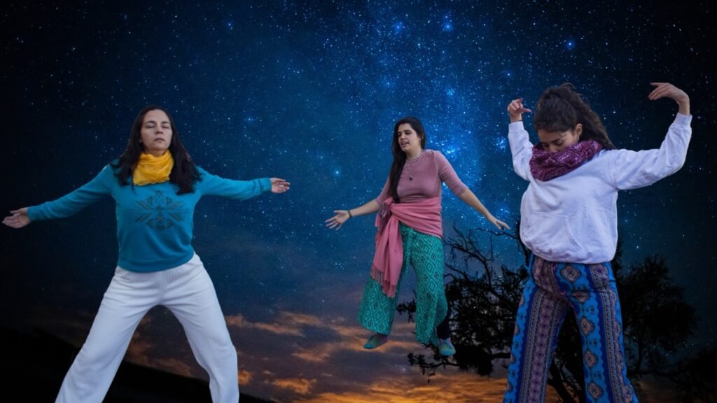 Tres mujeres bailando con los ojos cerrados bajo un cielo estrellado. Fotografia de Micaela Burgos