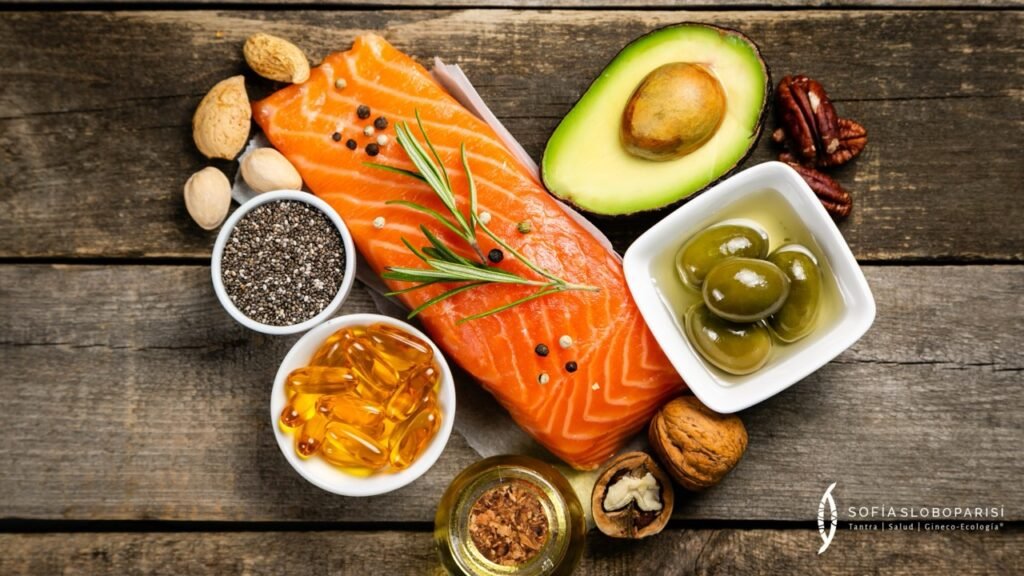 Alimentos saludables ricos en grasas buenas, con salmón, aguacate, aceite de oliva, semillas y frutos secos sobre mesa de madera